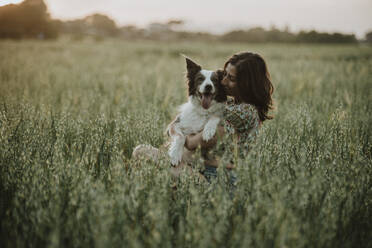 Frau umarmt und küsst Border Collie Hund im Feld bei Sonnenuntergang - GMLF01427