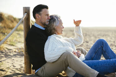 Woman shielding eyes sitting with man at beach - EBSF03197