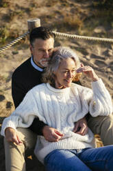 Man sitting with woman shielding eyes at beach - EBSF03199