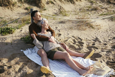 Mann und Frau sitzen auf einer Picknickdecke am Strand - EBSF03202