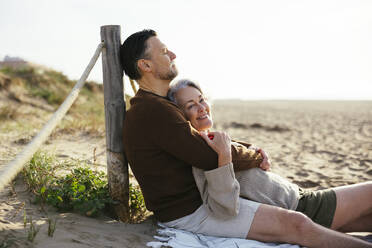 Man embracing woman sitting at beach - EBSF03203