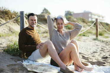 Frau mit Hand im Haar neben Mann am Strand sitzend - EBSF03208