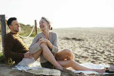 Happy woman talking to man sitting at beach - EBSF03209