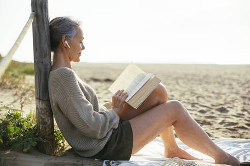 Reife Frau liest Buch am Strand sitzend - EBSF03211