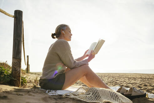 Reife Frau liest Buch an einem sonnigen Tag am Strand - EBSF03213