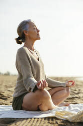 Woman meditating sitting on picnic blanket at beach - EBSF03218
