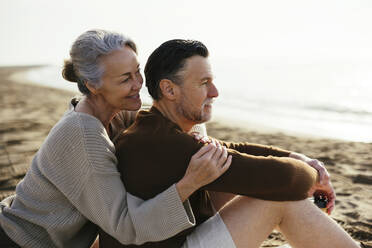 Lächelnde Frau umarmt Mann am Strand sitzend - EBSF03224