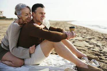 Lächelnde Frau umarmt Mann mit Einwegbecher am Strand - EBSF03225