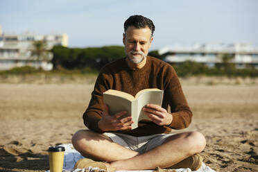 Man reading book sitting cross-legged at beach - EBSF03227