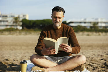 Mann liest Buch im Schneidersitz am Strand - EBSF03227