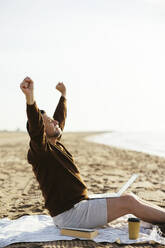 Man with laptop stretching hands at beach - EBSF03228