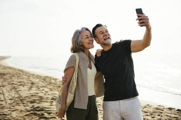 Ein Mann hält einen Moment mit seiner Begleiterin an einem malerischen Strand fest und posiert für ein Selfie - EBSF03235