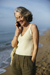 Happy woman talking on smart phone standing at beach - EBSF03238