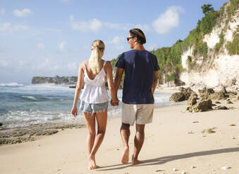 Happy young couple holding hands and walking at beach - IKF00165