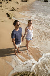 Glückliches junges Paar, das sich an den Händen hält, in der Nähe des Strandes stehend - IKF00170