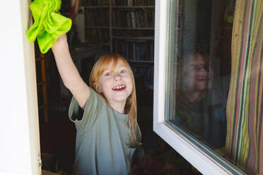 Smiling girl cleaning window at home - IHF01341