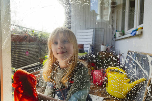 Lächelndes rothaariges Mädchen, das Fensterscheiben abwischt - IHF01347