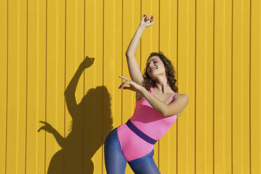 Carefree woman dancing in front of yellow wall - SYEF00344