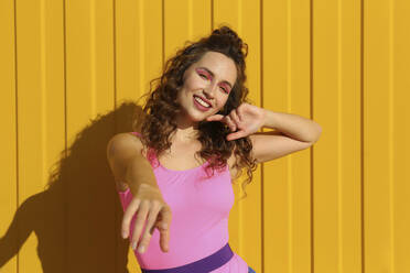 Smiling young woman wearing bodysuit dancing in front of yellow wall - SYEF00345