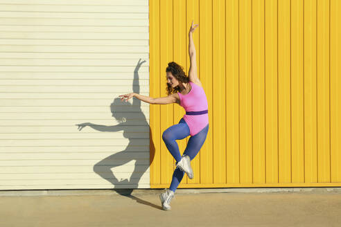 Young dancer showing ballet moves in front of yellow wall - SYEF00346