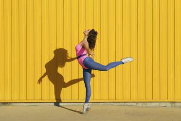Woman wearing bodysuit showing ballet moves in front of yellow wall - SYEF00348