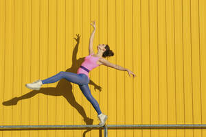 Unbekümmerte Frau übt Ballett auf dem Geländer vor einer gelben Wand - SYEF00356