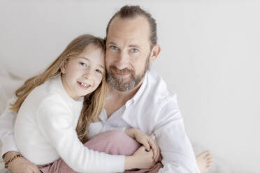 Father and daughter sitting near white wall - GMLF01433