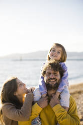 Lächelnde Frau betrachtet ihre Tochter, die auf den Schultern ihres Vaters am Strand sitzt - JOSEF18545