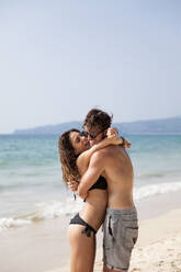 Man embracing woman wearing bikini at beach - IKF00179