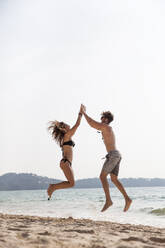 Happy couple giving high-five jumping at beach - IKF00180