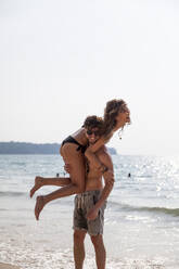 Man carrying girlfriend on shoulder at beach - IKF00183