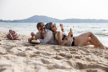 Happy couple spending leisure time lying on sand at beach - IKF00187