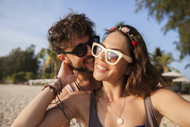 Happy couple wearing sunglasses at beach - IKF00191