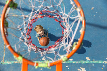 Boy standing with basketball under hoop at sports court - IKF00203