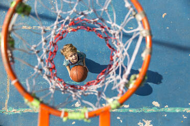 Junge stehend mit Basketball unter dem Basketballkorb auf dem Sportplatz - IKF00203