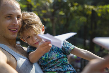 Vater und Sohn spielen mit Papierflugzeug an einem sonnigen Tag - IKF00210