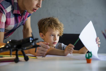 Vater unterrichtet Sohn am Schreibtisch sitzend zu Hause - IKF00215