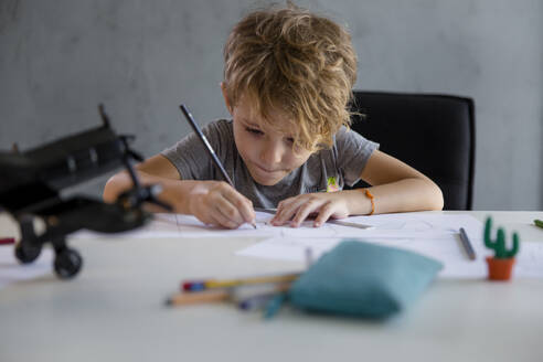 Junge mit Bleistift schreibt auf Papier am Schreibtisch - IKF00217