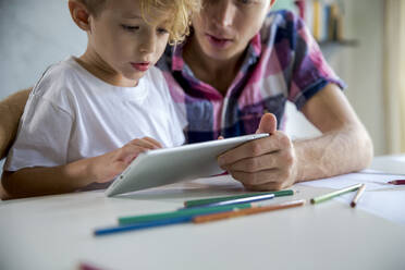 Vater und Sohn benutzen einen Tablet-PC am Schreibtisch - IKF00221