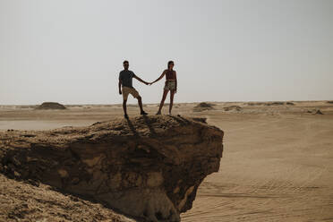 Couple holding hands and standing on rock in desert - GMLF01446