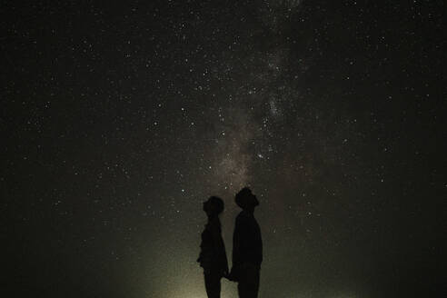 Silhouette eines Paares, das nachts vor den Sternen steht - GMLF01454