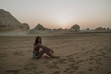 Frau sitzt auf Sand in der Wüste bei Sonnenuntergang - GMLF01458