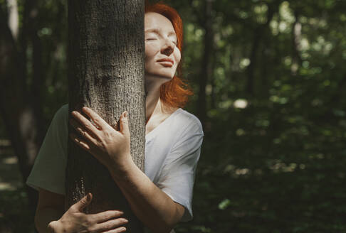 Frau umarmt Baum im Wald an einem sonnigen Tag - AZF00512