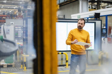 Thoughtful man standing with tablet PC in factory - DIGF19897