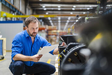 Mature businessman with document examining machine at factory - DIGF19934