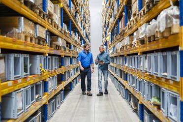 Businessman and manager walking between aisle in warehouse - DIGF19947