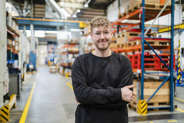 Smiling young employee with arms crossed at factory - DIGF19987