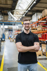 Employee wearing eyeglasses standing with arms crossed at factory - DIGF19993