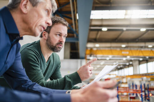 Manager pointing by businessman leaning on railing at factory - DIGF20011