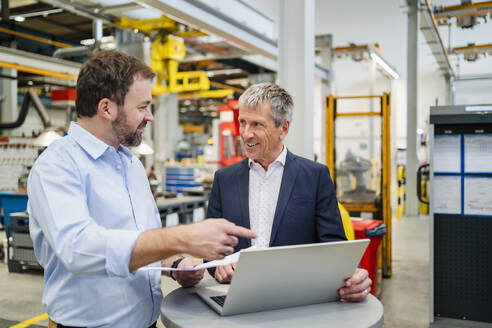 Manager zeigt auf Laptop von Geschäftsmann in Fabrik - DIGF20021
